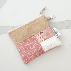 Op de afbeelding: Kleine patchwork etui met ritssluiting in lichtroze en goud. De etui heeft een stippenpatroon, een teckelprint en een klein label met de tekst "PETUNIAS by kelly". Het heeft een kleine lus en een zilveren sluiting.