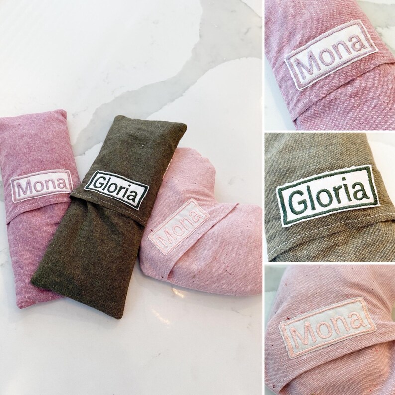 Peut inclure: Trois articles en tissu dans les tons de rose et vert olive, chacun avec un patch rectangulaire blanc brod&eacute; d'un nom. Les noms "Mona" et "Gloria" sont visibles. Les articles semblent &ecirc;tre de petits oreillers ou pochettes.