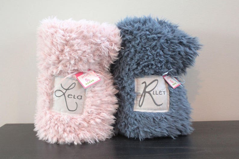 May include: Two personalised fluffy blankets, one pink with the name "Ela" and one grey with the name "Riley".