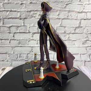 K&ouml;nnte beinhalten: Figur einer Figur in einem dunkelvioletten Outfit mit langem Umhang, die auf einer schwarz-roten Basis steht. Die Figur hat eine Kapuze und goldene Akzente. Die Basis hat schach&auml;hnliche Teile.