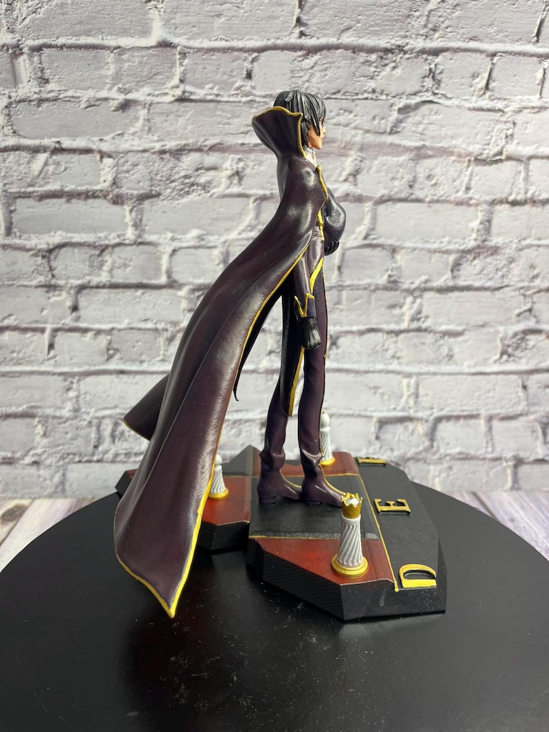 K&ouml;nnte beinhalten: Detaillierte Figur einer Figur in einem langen, dunkelvioletten Mantel mit goldenen Verzierungen. Die Figur steht auf einem schwarz-roten Sockel mit goldenen Akzenten. Die Figur hat schwarzes Haar und ist im Seitenprofil dargestellt.