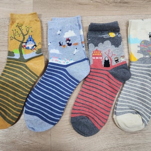 Può includere: Quattro paia di calzini a righe colorate con diversi personaggi dei cartoni animati stampati su di essi. I calzini presentano personaggi di film d'animazione popolari, tra cui Totoro, Kiki consegne a domicilio e La città incantata.