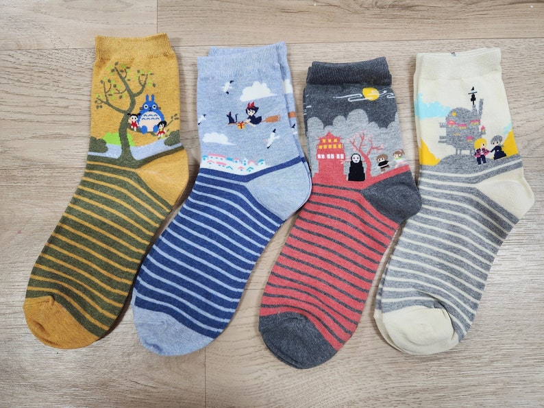 K&ouml;nnte beinhalten: Vier Paar bunte, gestreifte Socken mit verschiedenen Comicfiguren darauf gedruckt. Die Socken zeigen Figuren aus beliebten Animationsfilmen, darunter Totoro, Kiki liefert aus und Chihiros Reise ins Zauberland.