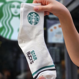 May include: White socks with a green Starbucks logo and the text "STARBUCKS" in green and black lettering.