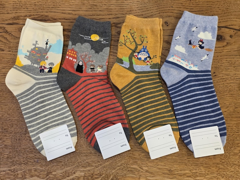 May include: Four pairs of crew socks with cartoon designs. Each pair has a different design, including a castle, a character with a mask, a tree with characters, and a witch on a broom. The socks have striped patterns in various colors.