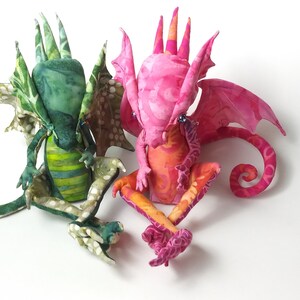 May include: Two handmade fabric dragons, one green and one pink, with detailed wings and curled tails.
