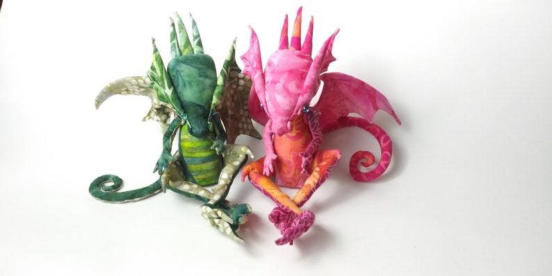 May include: Two handmade fabric dragons, one green and one pink, with detailed wings and curled tails.