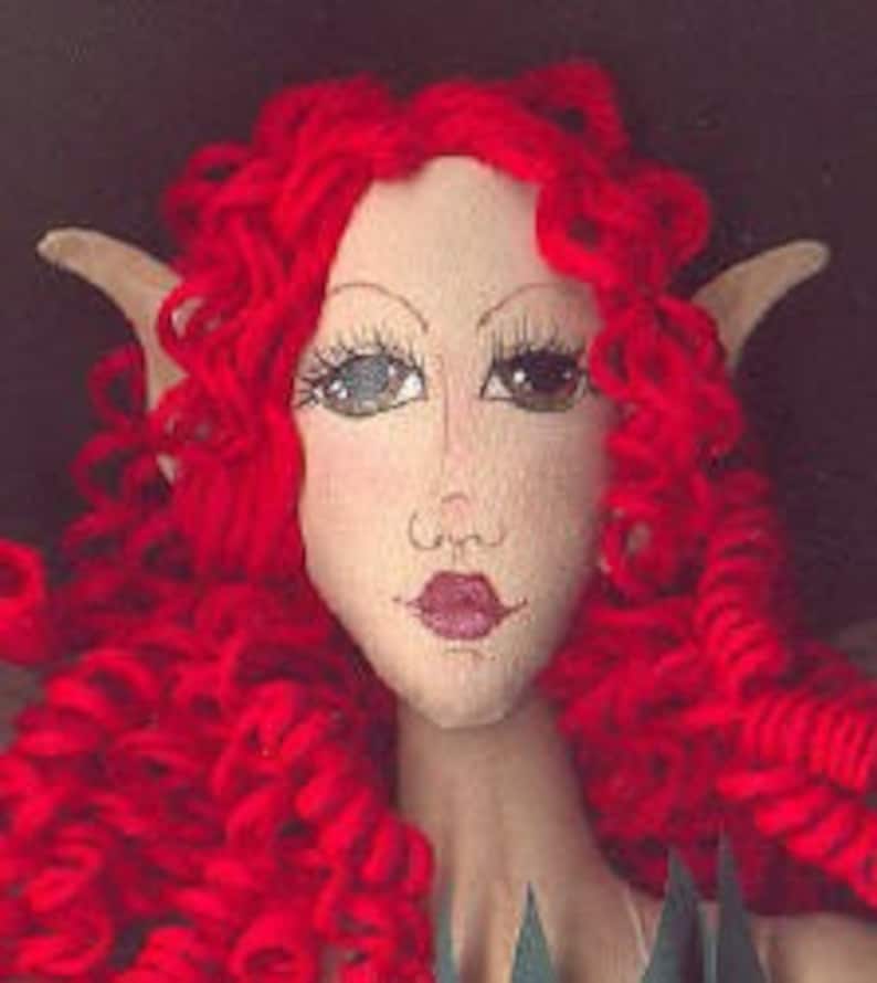 Pu&ograve; includere: Una bambola fatta a mano con capelli rossi ricci, orecchie a punta e un viso dipinto. La bambola ha occhi marroni, una bocca rosa e un incarnato chiaro.