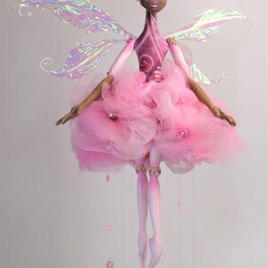 May include: A pink fairy doll with iridescent wings, a pink tulle skirt, and pink and gold beads hanging from her legs.