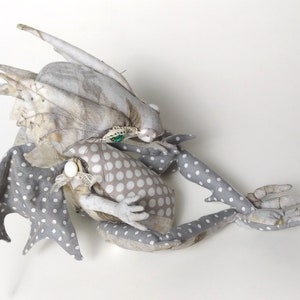 May include: A gray and white fabric dragon with polka dot wings and a floral patterned body. The dragon is curled up with its head resting on its body.