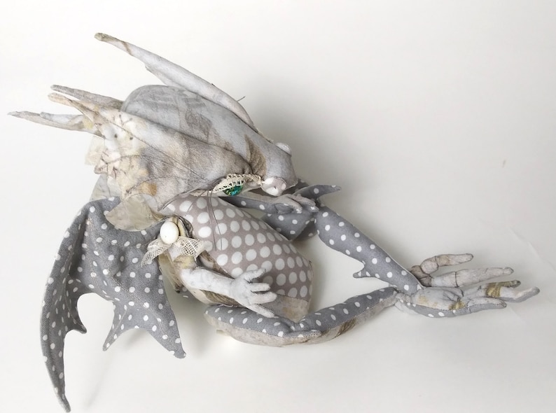 May include: A gray and white fabric dragon with polka dot wings and a floral patterned body. The dragon is curled up with its head resting on its body.