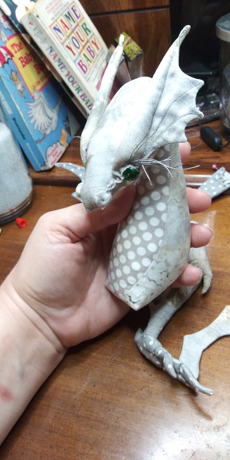 May include: A white and gray fabric dragon with a green eye and white polka dots. The dragon has large ears and a long tail.