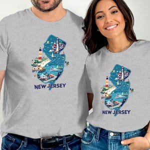 May include: Two grey t-shirts with a graphic of the state of New Jersey, featuring a blue outline of the state with various landmarks and the text "NEW JERSEY" printed below.