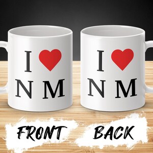 May include: White ceramic coffee mug with a red heart and the text "I love NM" on the front and back.