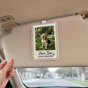 Puede incluir: Un clip de acrílico transparente para visera de coche con una foto rectangular de un beagle sentado sobre hierba verde. La parte inferior de la inserción muestra el texto negro Drive Safe y LOVE GIANNA con un pequeño icono de huella.