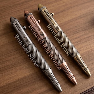 May include: Three bolt-action pens with a textured, spiraled grip and a smooth upper barrel. The pens are labeled Brushed Silver, Brushed Red Bronze, and Brushed Brass. Each pen features a metal pocket clip, a bolt-action mechanism, and a pointed tip.