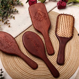 May include: Four wooden hairbrushes with engraved designs. One brush is rectangular with wooden bristles, while the others are oval-shaped. The brushes are a dark reddish-brown color, with personalized text and floral accents.