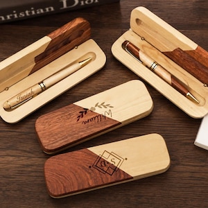 May include: Two open wooden pen cases containing light-colored wooden pens, one engraved with the name Isaiah, and two closed wooden pen cases featuring diagonal wood grain patterns, one engraved with the name William and one with the initials SD.