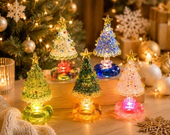 May include: Five miniature glass Christmas tree figurines with textured branches and a yellow star topper. Each tree sits on a rounded, translucent base that glows with internal light in colors including green, blue, pink, and clear.