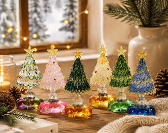 May include: Six miniature glass Christmas trees with textured, colorful branches and a clear star topper. Each tree sits on a matching colored glass base. The trees are arranged in a row, featuring clear, pink, dark green, yellow, green, and blue colors.