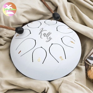 May include: White handpan with eight notes, a black mallet, and the name "Kally" inscribed on the top.
