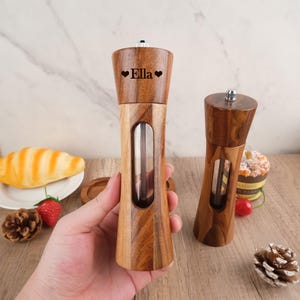 May include: Two wooden salt and pepper shakers with clear glass inserts. The shaker on the left is personalized with the name "Ella" and two hearts.