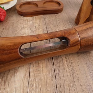 May include: A wooden pepper mill with a clear glass window to view the peppercorns inside. The mill has a stainless steel grinding mechanism.