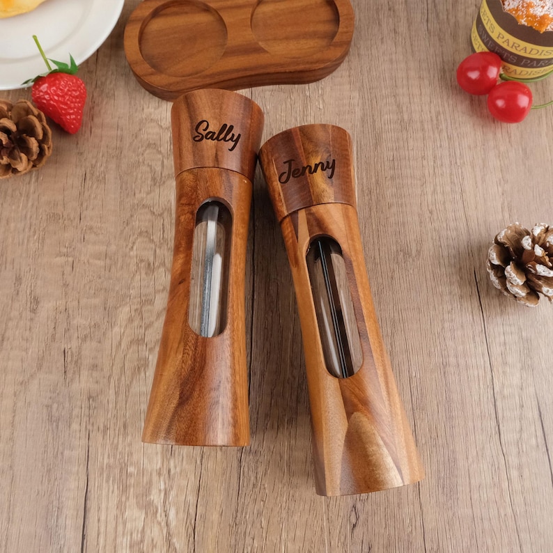 May include: Two wooden salt and pepper shakers with clear glass inserts. The shakers are engraved with the names "Sally" and "Jenny".
