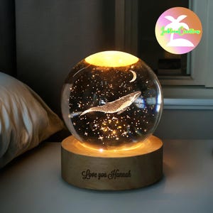 May include: A glass globe night light featuring a whale and stars design. The base is made of wood and is inscribed with the words "Love you Hannah".