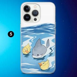 May include: A clear phone case featuring a cartoon shark swimming in blue water with two yellow ducks. The case has a white border and a black number 5 in a circle.