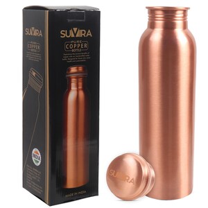 Puede incluir: Una botella de agua de cobre con una tapa de rosca a juego, junto a su caja negra. La caja presenta la marca "SUVIRA" y las palabras "PURE COPPER BOTTLE". La botella y la tapa tienen un acabado met&aacute;lico brillante. La caja tambi&eacute;n dice "MADE IN INDIA".