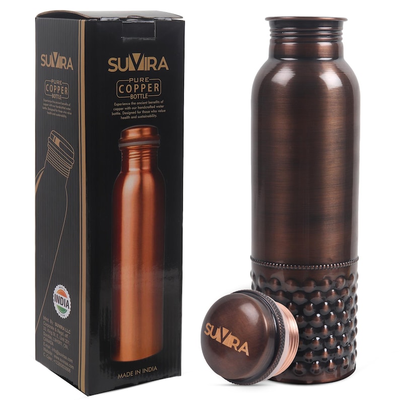 Puede incluir: Una botella de agua de cobre con tapa a juego y base decorativa. La botella est&aacute; junto a su caja negra original, que presenta la marca "SUVIRA" y las palabras "Pure Copper Bottle."