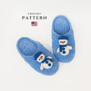 Peut inclure: Une paire de pantoufles en crochet bleu avec une applique de bonhomme de neige sur chaque pantoufle. Les pantoufles sont faites avec un fil moelleux et ont un design simple. CROCHET PATTERN est écrit en noir au-dessus d'un petit drapeau américain.