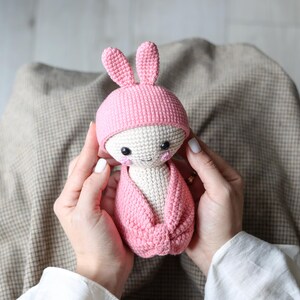 May include: A pink crocheted bunny doll with a white face and black eyes. The doll is wearing a pink crocheted hat with bunny ears.