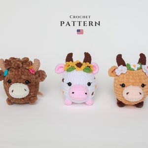 以下が含まれることがあります： 茶色、白、ベージュの3つの編み物牛のぬいぐるみ。それぞれにユニークな花の冠が付いています。「CROCHET PATTERN」の文字が牛の上にあり、小さなアメリカ国旗があります。 赤ちゃんの部屋に最適です。