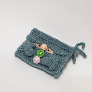May include: A blue crocheted gnome pouch with a small gnome face peeking out. The pouch has three buttons, two green and one pink.