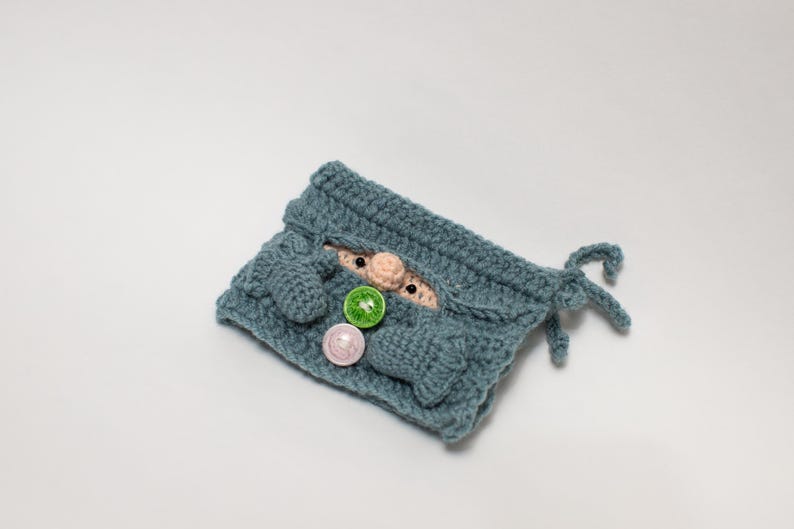 May include: A blue crocheted gnome pouch with a small gnome face peeking out. The pouch has three buttons, two green and one pink.