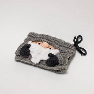 May include: Gray crocheted pouch with a black drawstring. The pouch features a crocheted face of a gnome with a white beard and black eyes.