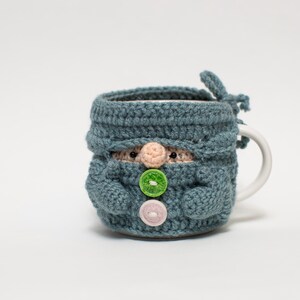 May include: A blue crocheted mug cozy shaped like a gnome with green and pink buttons.