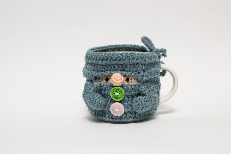 May include: A blue crocheted mug cozy shaped like a gnome with green and pink buttons.