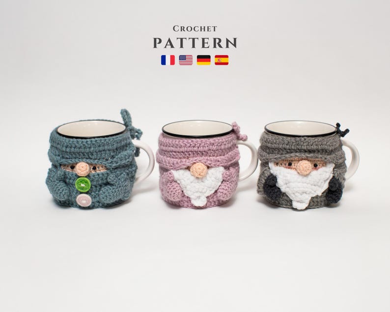 May include: Three crocheted mug cozies in the shape of gnomes. The cozies are in blue, pink, and gray. The cozies have white beards and black eyes. The text "CROCHET PATTERN" is above the cozies.