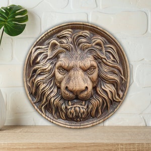 Può includere: Una scultura da parete in legno di una testa di leone con una scultura dettagliata della criniera e dei tratti del viso. La scultura è dipinta di colore marrone scuro e ha una forma circolare.