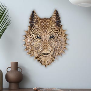 May include: A detailed wooden wolf head wall sculpture. The carving showcases elaborate patterns and a textured finish. The wolf's eyes are dark, and the overall colour is a warm, golden brown. This decorative piece adds a rustic touch to any space.