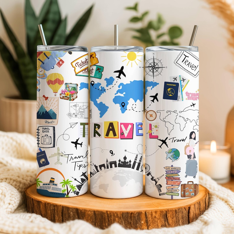 K&ouml;nnte beinhalten: Drei wei&szlig;e Reisebecher mit silbernen Strohhalmen. Jeder Becher zeigt Illustrationen zum Thema Reisen, darunter Flugzeuge, Karten und das Wort "TRAVEL". Ein Becher hat eine Weltkarte in Blau. Die Becher werden auf einer Holzoberfl&auml;che pr&auml;sentiert.