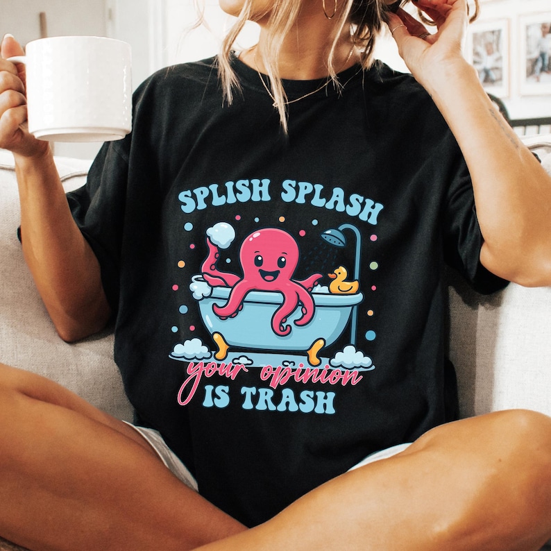 May include: A black t-shirt featuring a graphic of a pink octopus in a light blue bathtub with a yellow rubber duck, bubbles, and a shower head. The text reads "SPLISH SPLASH" in light blue and "your opinion IS TRASH" in pink and light blue.