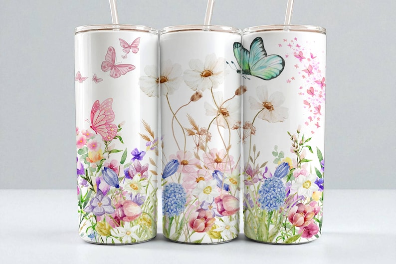 May include: Three white stainless steel tumblers with floral and butterfly designs. The tumblers feature watercolor illustrations of pink and purple flowers, butterflies, and greenery. Each tumbler has a clear straw.