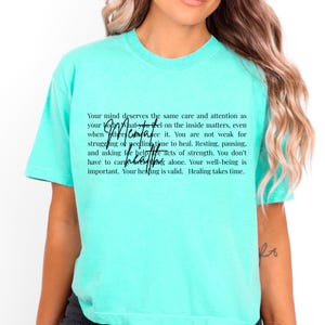 May include: A light turquoise t-shirt with the text "Your mind deserves the same care and attention as your body. What you feel on the inside matters, even when others can't see it." The shirt has a crew neck and short sleeves.