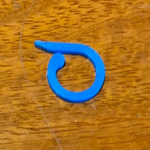 May include: A bright blue plastic ring, shaped like a circle with a small gap in the top. The ring is on a wooden surface.