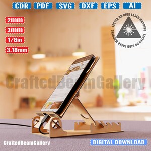 Puede incluir: Un soporte de tel&eacute;fono de madera con un tel&eacute;fono apoyado en &eacute;l. El soporte est&aacute; dise&ntilde;ado para sostener un tel&eacute;fono en posici&oacute;n vertical y tiene una ranura para cables de carga. El soporte est&aacute; hecho de madera marr&oacute;n claro y tiene un dise&ntilde;o simple. El tel&eacute;fono es un tel&eacute;fono inteligente negro con una pantalla que muestra un sitio web. El soporte est&aacute; sobre una mesa con un fondo borroso.