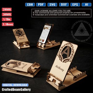 Könnte beinhalten: Ein Set aus lasergeschnittenen Handyhaltern aus Holz mit verzierten Monogrammen und Namen wie Naomi, Jessica und Anthony. Die Halter sind verstellbar mit mehreren Schlitzen und enthalten digitale Dateiformate wie CDR, PDF, SVG, DXF, EPS und AI.